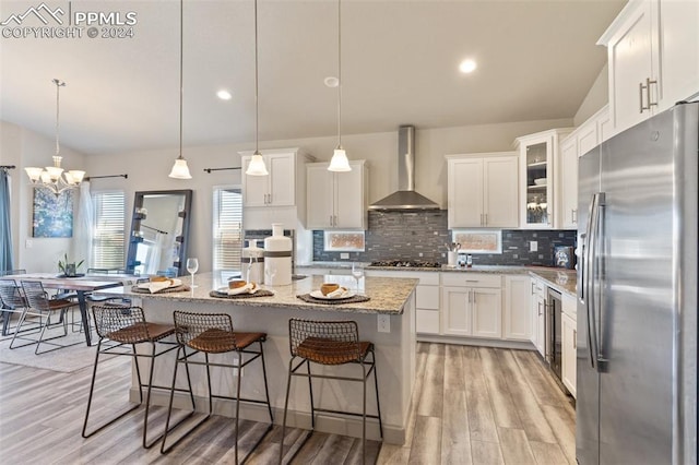 kitchen with wall chimney exhaust hood, stainless steel refrigerator with ice dispenser, a center island, decorative light fixtures, and white cabinets