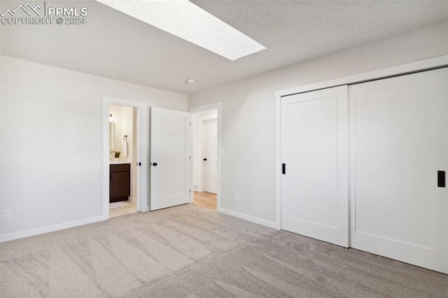 unfurnished bedroom with a skylight, a textured ceiling, connected bathroom, light colored carpet, and a closet