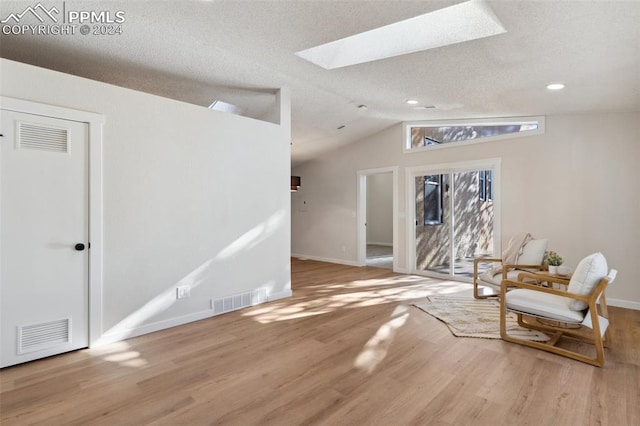 interior space featuring a textured ceiling, light hardwood / wood-style flooring, and vaulted ceiling with skylight