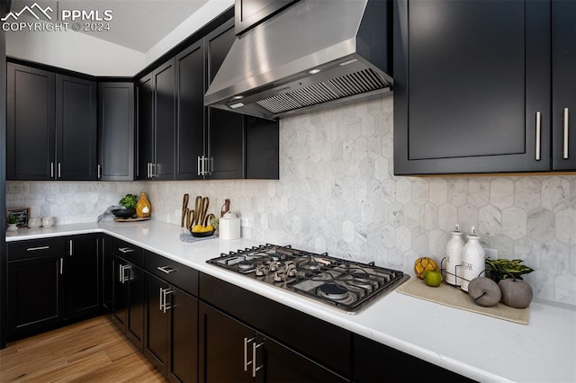 kitchen featuring decorative backsplash, wall chimney range hood, stainless steel gas cooktop, and light wood-type flooring