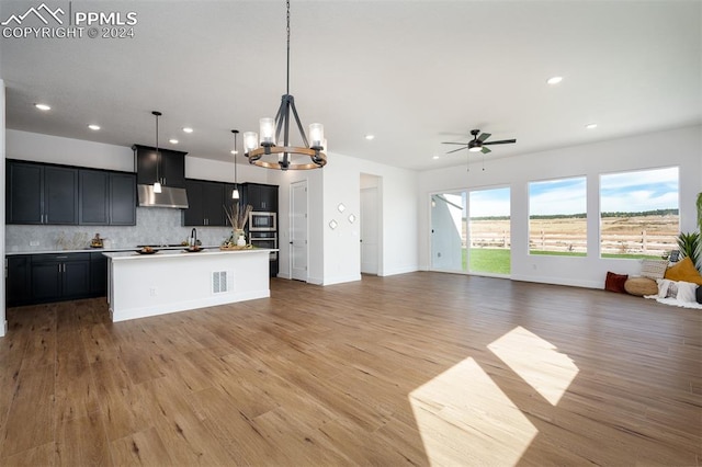 kitchen featuring decorative backsplash, a kitchen island with sink, decorative light fixtures, and light wood-type flooring