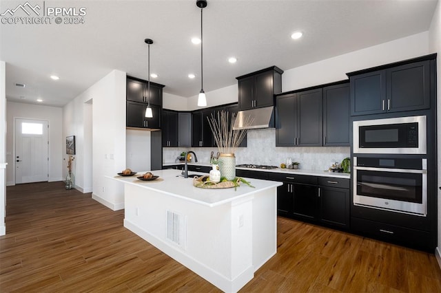 kitchen with a center island with sink, decorative backsplash, appliances with stainless steel finishes, and dark hardwood / wood-style floors