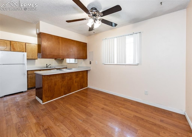 kitchen with white appliances, sink, light wood-type flooring, a textured ceiling, and kitchen peninsula