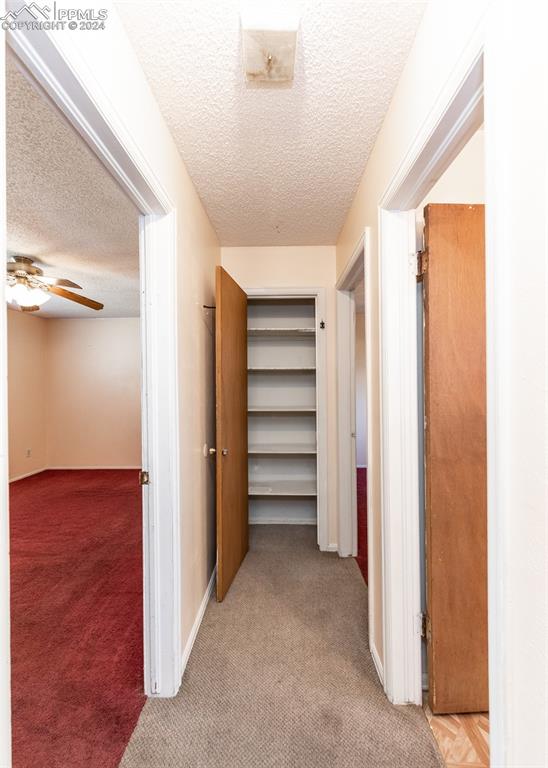 corridor with light carpet and a textured ceiling