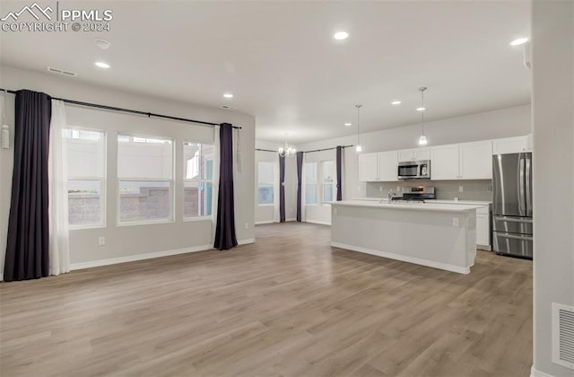 kitchen with appliances with stainless steel finishes, light hardwood / wood-style flooring, pendant lighting, and an island with sink