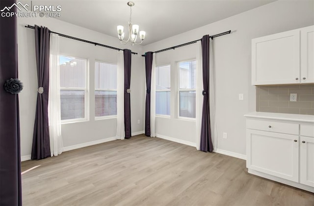 unfurnished dining area with an inviting chandelier and light wood-type flooring