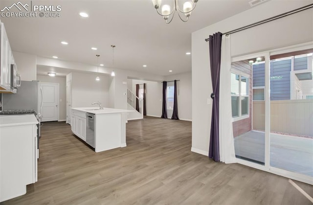 kitchen with wood-type flooring, sink, decorative light fixtures, white cabinets, and a center island with sink