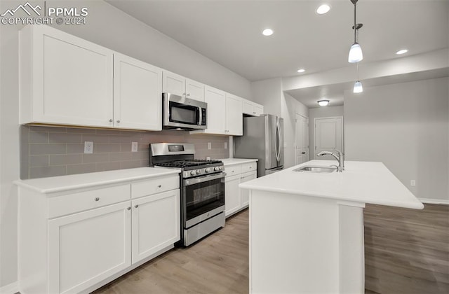 kitchen with an island with sink, hanging light fixtures, stainless steel appliances, sink, and light hardwood / wood-style floors