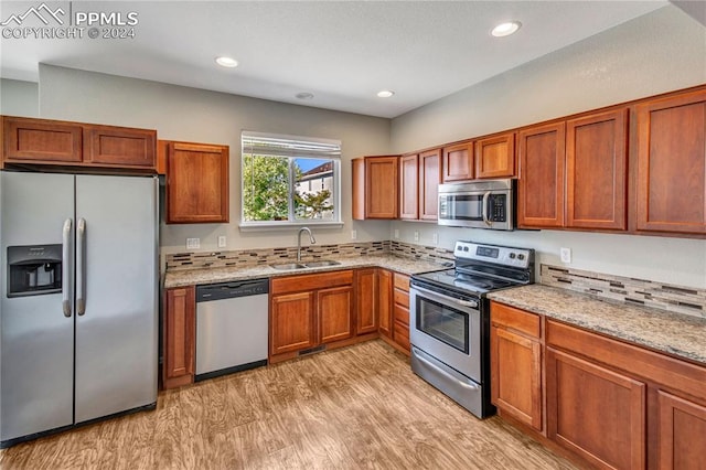 kitchen with sink, light stone countertops, stainless steel appliances, and light wood-type flooring