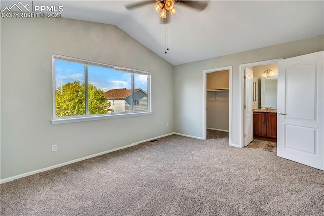 unfurnished bedroom with ceiling fan, a spacious closet, connected bathroom, vaulted ceiling, and light colored carpet