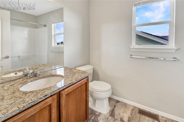 bathroom featuring a healthy amount of sunlight, vanity, toilet, and walk in shower