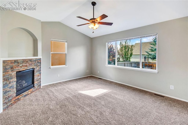 unfurnished living room featuring carpet, vaulted ceiling, a stone fireplace, and ceiling fan