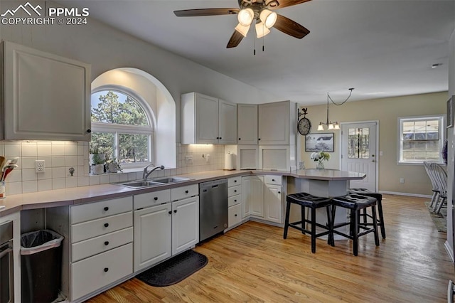 kitchen featuring dishwasher, ceiling fan with notable chandelier, light hardwood / wood-style floors, white cabinets, and decorative backsplash