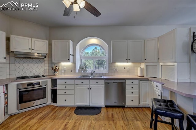 kitchen with decorative backsplash, sink, white cabinets, light wood-type flooring, and appliances with stainless steel finishes