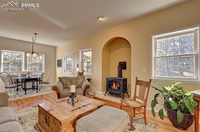 living room with a wood stove, a healthy amount of sunlight, a chandelier, and light wood-type flooring