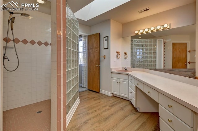 bathroom featuring vanity, hardwood / wood-style flooring, a skylight, and tiled shower