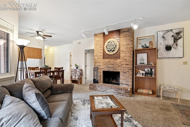 living room featuring ceiling fan, rail lighting, a textured ceiling, a brick fireplace, and carpet floors