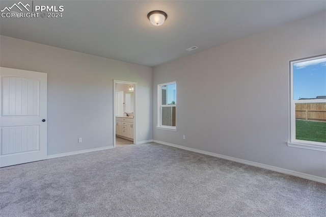 unfurnished bedroom featuring light carpet and ensuite bath