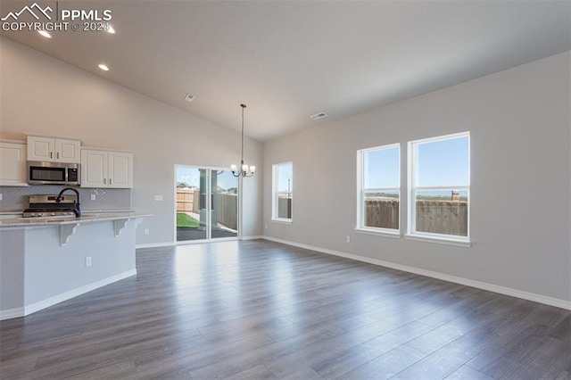 unfurnished living room featuring high vaulted ceiling, an inviting chandelier, and dark hardwood / wood-style floors