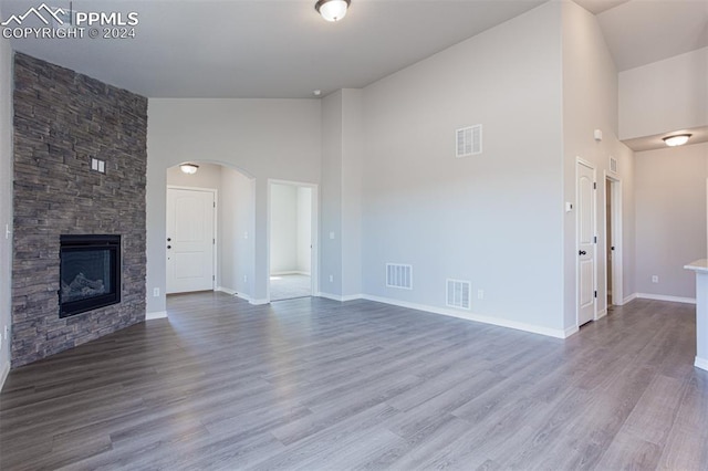 unfurnished living room featuring a stone fireplace, high vaulted ceiling, and wood-type flooring