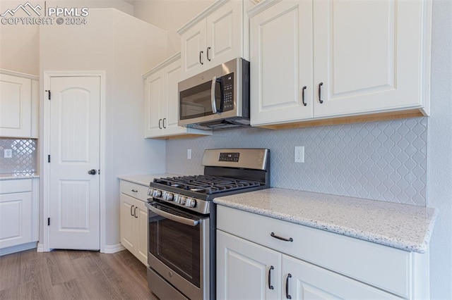 kitchen featuring white cabinets, tasteful backsplash, appliances with stainless steel finishes, light stone countertops, and light hardwood / wood-style flooring