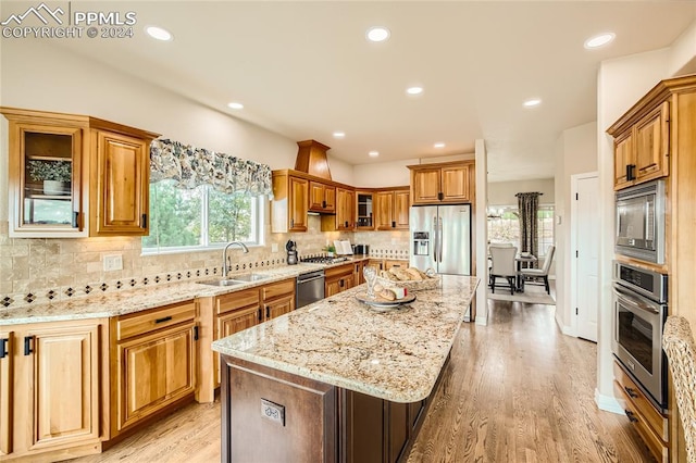 kitchen with a kitchen island, sink, light stone countertops, appliances with stainless steel finishes, and light hardwood / wood-style floors