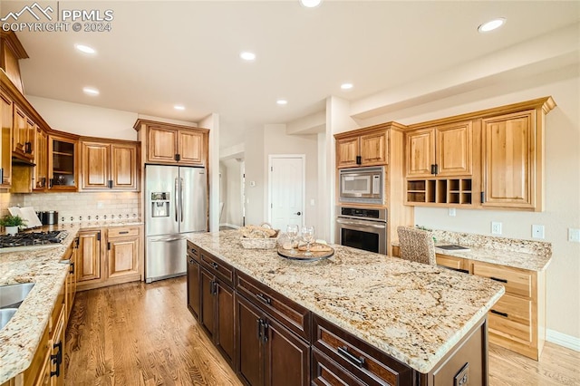 kitchen featuring light stone countertops, a center island, appliances with stainless steel finishes, and light wood-type flooring