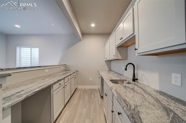 kitchen with white cabinetry, light stone counters, sink, and light wood-type flooring