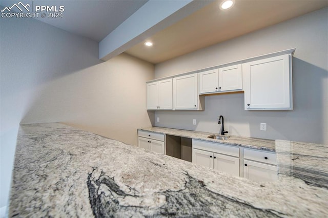 kitchen with dishwasher, beam ceiling, sink, light stone countertops, and white cabinetry