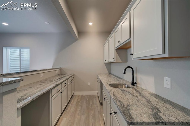 kitchen with light hardwood / wood-style floors, white cabinetry, sink, and light stone counters