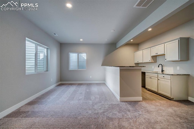 kitchen with light stone countertops, sink, kitchen peninsula, and light colored carpet