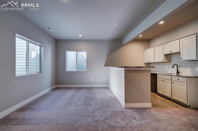 kitchen with sink, kitchen peninsula, white cabinetry, light carpet, and dark stone countertops