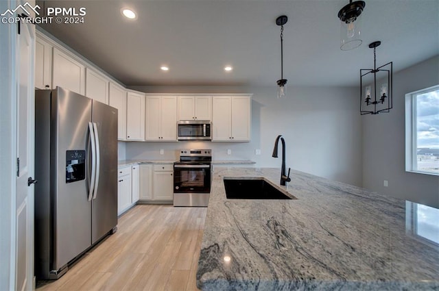 kitchen with hanging light fixtures, light stone counters, appliances with stainless steel finishes, white cabinetry, and sink