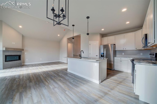 kitchen featuring lofted ceiling, an island with sink, white cabinetry, stainless steel appliances, and decorative light fixtures