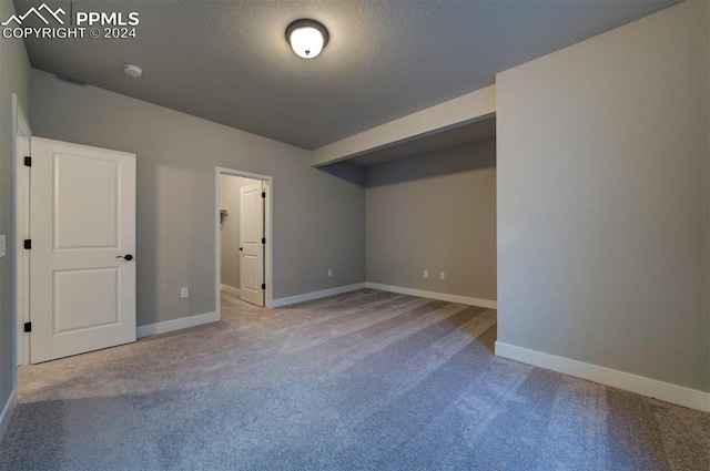 unfurnished bedroom featuring a spacious closet, a closet, a textured ceiling, and light colored carpet