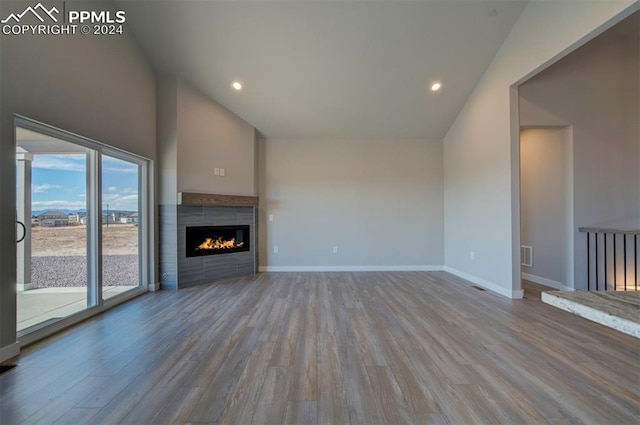 unfurnished living room featuring high vaulted ceiling, a tiled fireplace, and light hardwood / wood-style floors