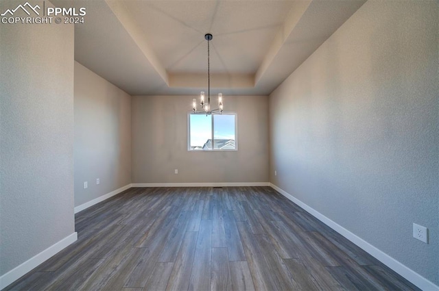 unfurnished dining area with dark wood-type flooring, an inviting chandelier, and a raised ceiling