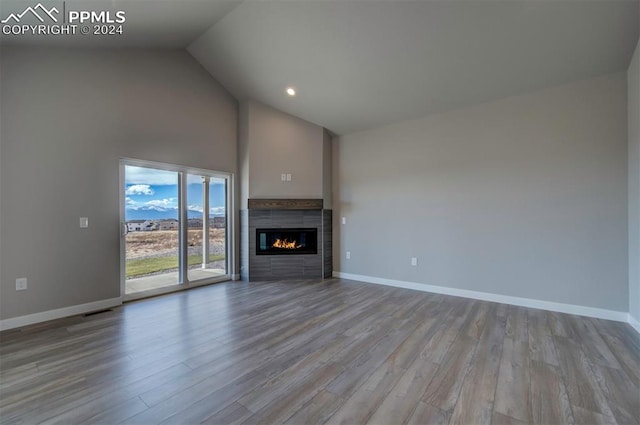 unfurnished living room featuring a tiled fireplace, light hardwood / wood-style floors, and high vaulted ceiling