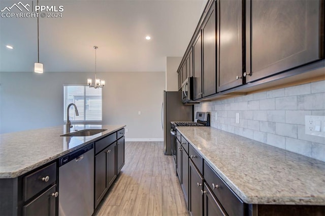 kitchen with an island with sink, appliances with stainless steel finishes, light wood-type flooring, sink, and decorative light fixtures