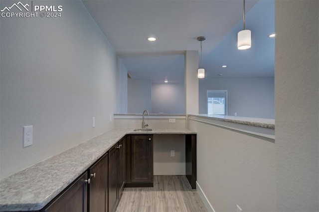 bar featuring sink, light stone countertops, dark brown cabinetry, decorative light fixtures, and light hardwood / wood-style floors