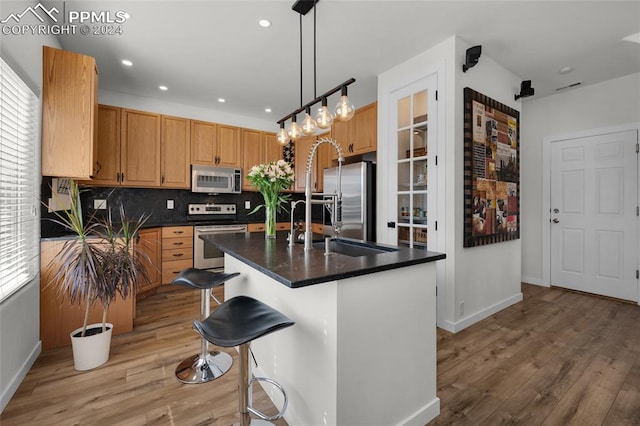 kitchen with decorative backsplash, hardwood / wood-style floors, appliances with stainless steel finishes, a kitchen island with sink, and decorative light fixtures