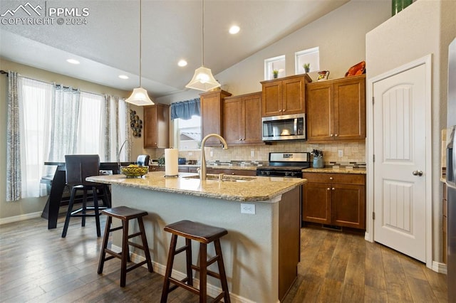 kitchen featuring dark hardwood / wood-style flooring, stainless steel appliances, vaulted ceiling, pendant lighting, and a center island with sink