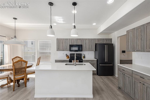 kitchen featuring decorative backsplash, a kitchen island with sink, black appliances, pendant lighting, and light hardwood / wood-style floors