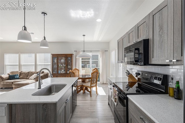 kitchen featuring decorative backsplash, a center island with sink, black appliances, pendant lighting, and sink