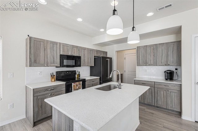 kitchen with a kitchen island with sink, sink, black appliances, pendant lighting, and light hardwood / wood-style floors