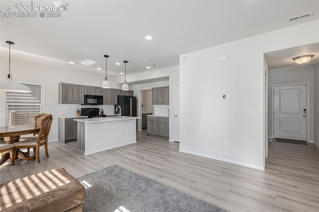 kitchen with black appliances, decorative light fixtures, a center island with sink, and light wood-type flooring