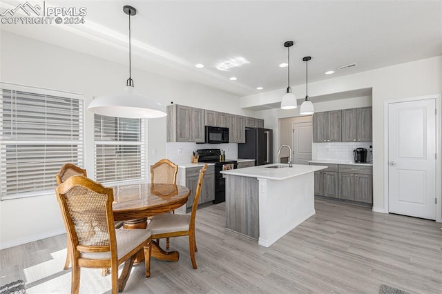 kitchen with light hardwood / wood-style flooring, black appliances, decorative light fixtures, and a kitchen island with sink