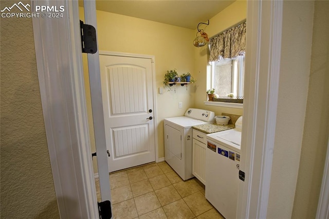 clothes washing area featuring washer and clothes dryer, light tile patterned floors, and cabinets