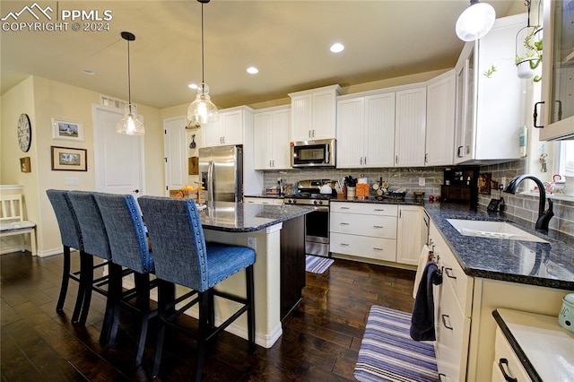 kitchen with appliances with stainless steel finishes, sink, a kitchen island, white cabinets, and dark hardwood / wood-style floors