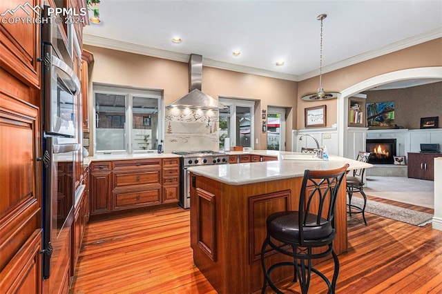 kitchen with stainless steel range, wall chimney exhaust hood, pendant lighting, a breakfast bar area, and a kitchen island with sink